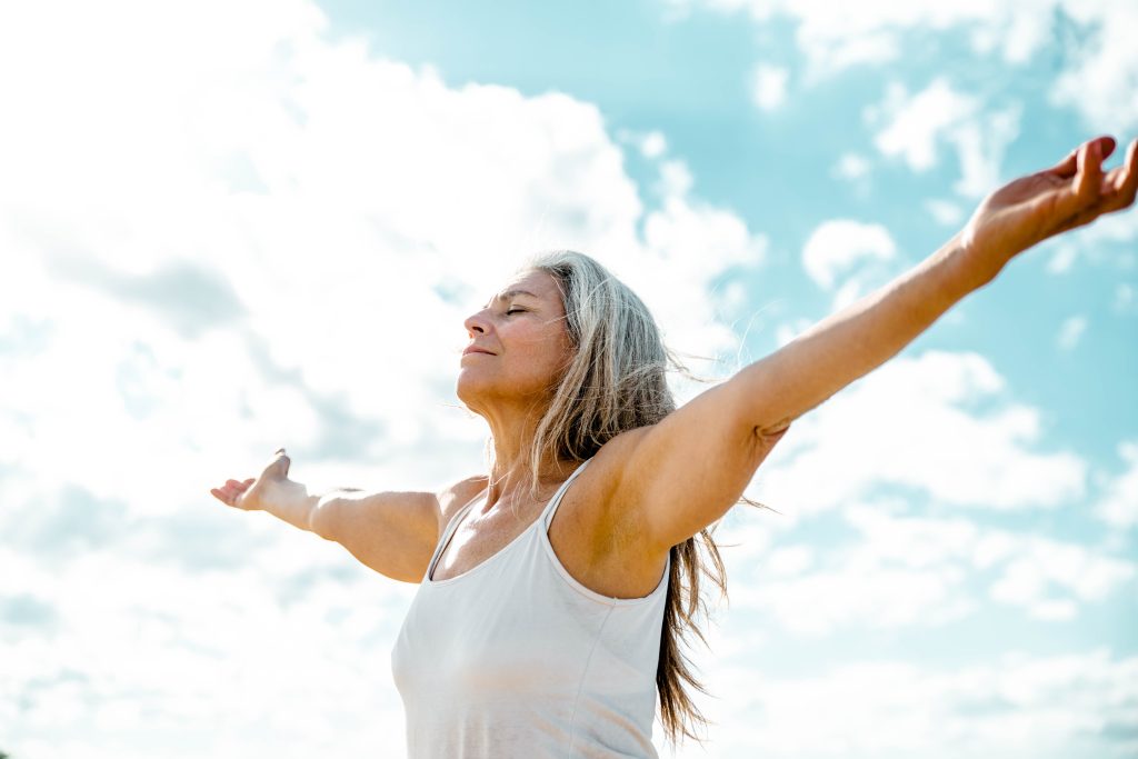 Joyful senior woman enjoying freedom standing with open arms and a content smile looking up towards the sky